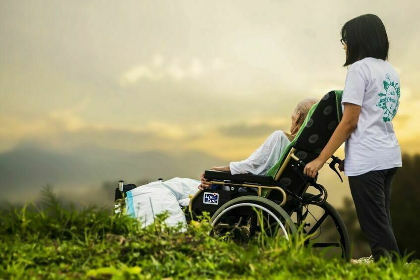 Dwie osoby, jedna z nich jest na wózku inwalidzkim, druga to opiekun.