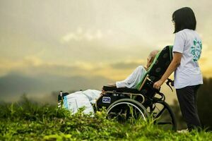 Dwie osoby, jedna z nich jest na wózku inwalidzkim, druga to opiekun.