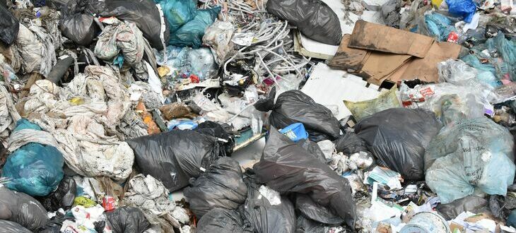 Zdjęcie przedstawia skupisko odpadów, w tym czarne worki na śmieci, porozrzucane plastiki i inne rodzaje odpadków, co wskazuje na problem zanieczyszczenia.