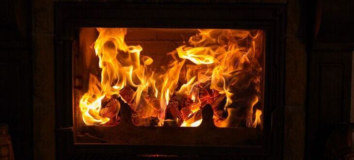 Płomienie ognia palą się w kominku, rozświetlając ciemność za pomocą ciepłego, jasnego światła.