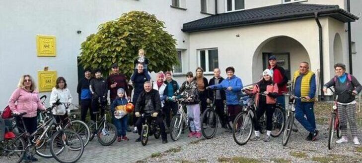 Grupa uśmiechniętych osób stoi przed budynkiem z rowerami, przygotowując się do wspólnej przejażdżki.