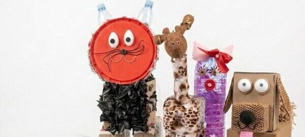 Trzy rzeźby ze zwierzętami wykonane z recyklingowych materiałów. Kot z butelek i kartonu, żyrafa z plastiku i szmatki oraz pies z pudełek i nakrętek. Każda postać ma duże oczy i przyjazny wyraz twarzy.