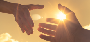 Dwie dłonie zbliżają się do siebie na tle słonecznego nieba, tworząc grę cieni i światła.