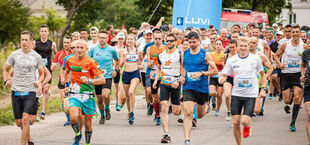 Grupa biegaczy uczestniczących w maratonie na asfaltowej drodze, niektórzy w koszulkach z numerami startowymi.