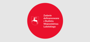 Czerwone koło z białym napisem i grafiką konia na tarczy, informujące o dofinansowaniu zadania z budżetu województwa lubelskiego.