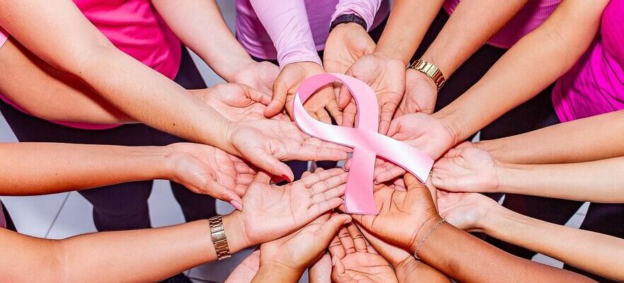 Grupa osób ułożyła dłonie razem, tworząc krąg wokół różowej wstążki, symbolu świadomości raka piersi.