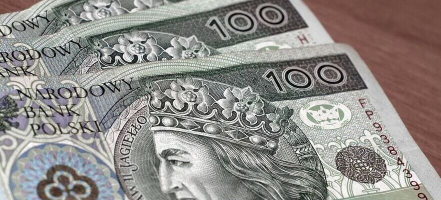 Stos banknotów o nominale 100 złotych ułożonych na drewnianym stole, z wizerunkiem króla Władysława Jagiełły na awersie.