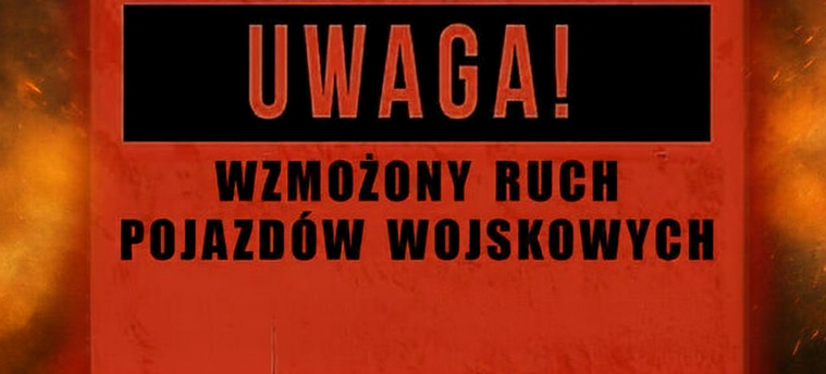 Czerwony znak ostrzegawczy z napisem "Uwaga! Wzmożony ruch pojazdów wojskowych". W tle widać pomarańczowe światła, przypominające płomienie.