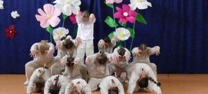 Dzieci przebrane za kwiaty, układające się w artystyczną kompozycję, z naśladując kwitnące pąki w tle sceny.