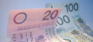 Polskie banknoty o nominałach 20 i 100 złotych leżące na przekątnej z przeważającym kolorem różowym dla dwudziestki i zielonym dla setki, na niebieskim tle.