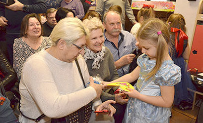 Dziewczynka wręcza babci prezent w tle grupa osób