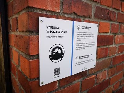 Tablica informacyjna umieszczona na ścianie zabytkowej studni w Pożarzysku