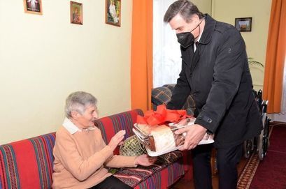 Burmistrz Leszek Michalak wręcza prezent na ręce stulatki