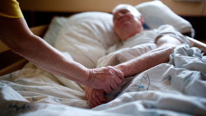 Pacjent leżący na łóżku i trzymająca go dłoń