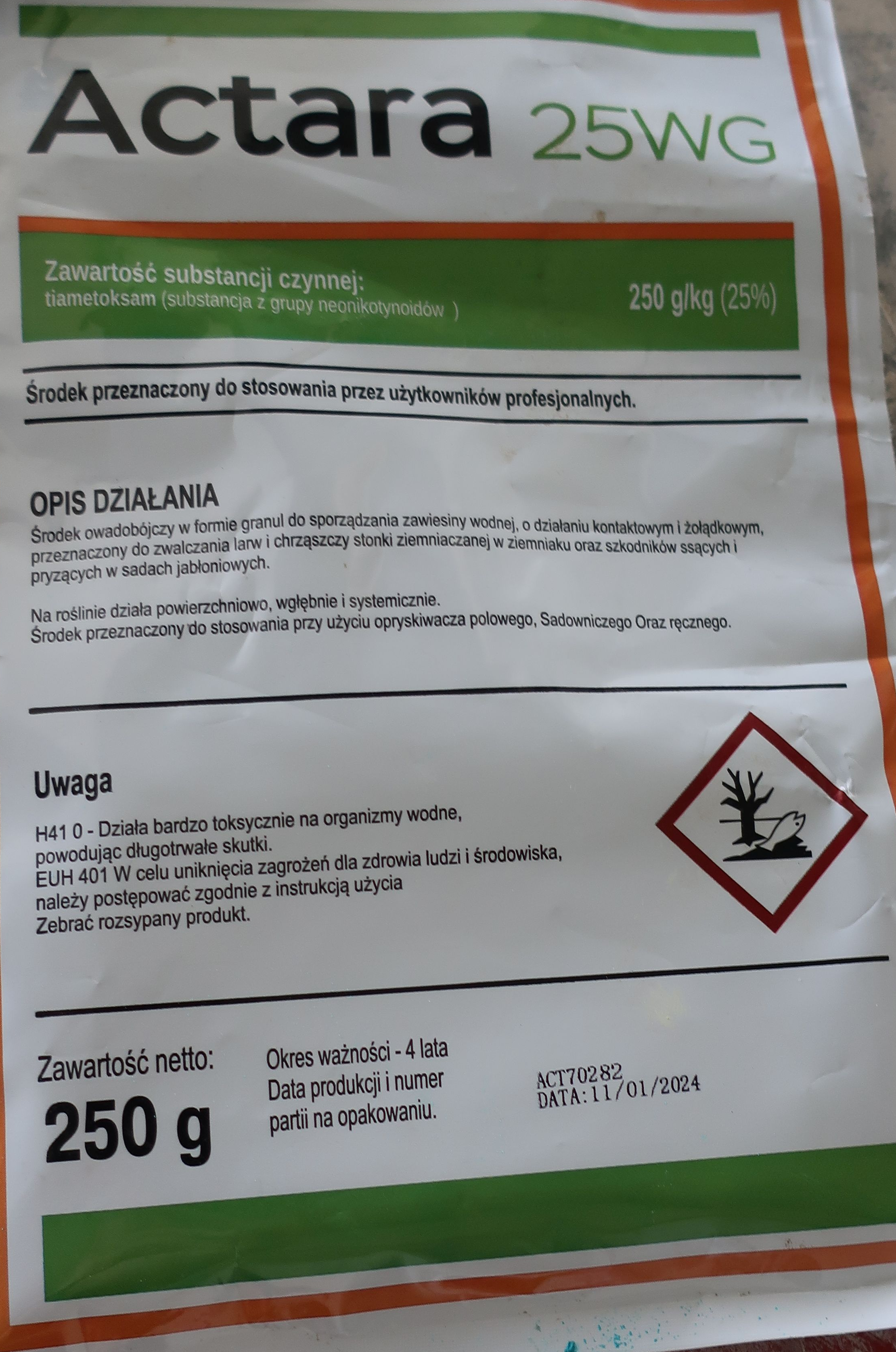 Opis alternatywny: Opakowanie leku w zielonym kolorze z białym i pomarańczowym tekstem, ostrzeżeniem przed zagrożeniem dla zdrowia i symbolami ostrzegawczymi.