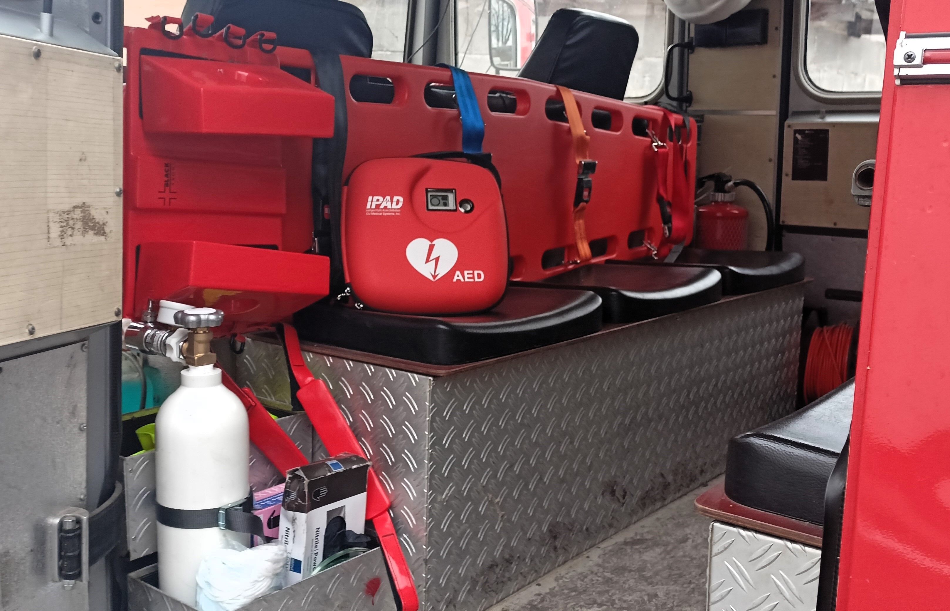 Defibrylator AED w czerwonej torbie z logotypem znajduje się w środku pojazdu obok czerwonych opakowań medycznych i aparatury ratunkowej.