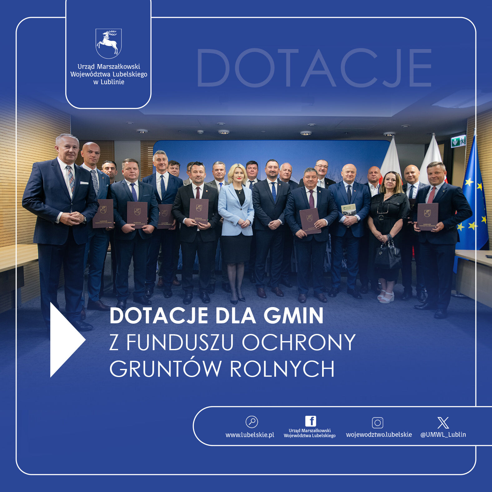 Grupa ludzi stoi w dwóch rzędach z dyplomami, za nimi baner z napisem "Dotacje dla gmin z funduszu ochrony gruntów rolnych".