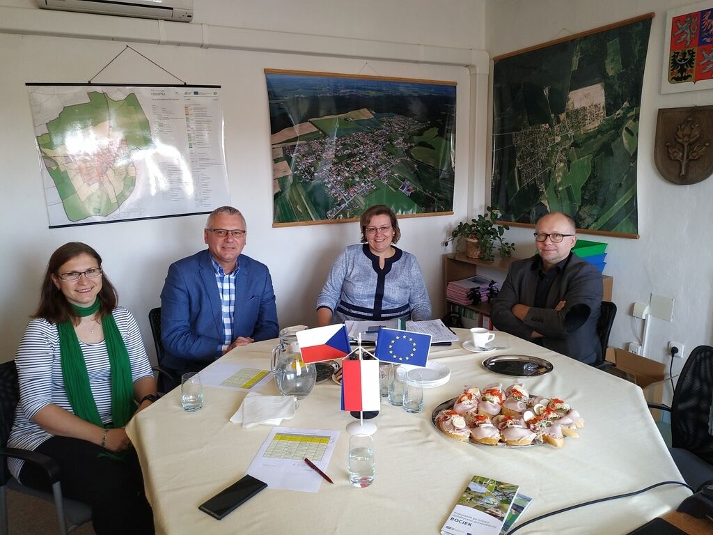 Cztery osoby usiadły przy stole z flagami Unii Europejskiej i Polski, naprzeciw map. Na stole kawa i przekąski.