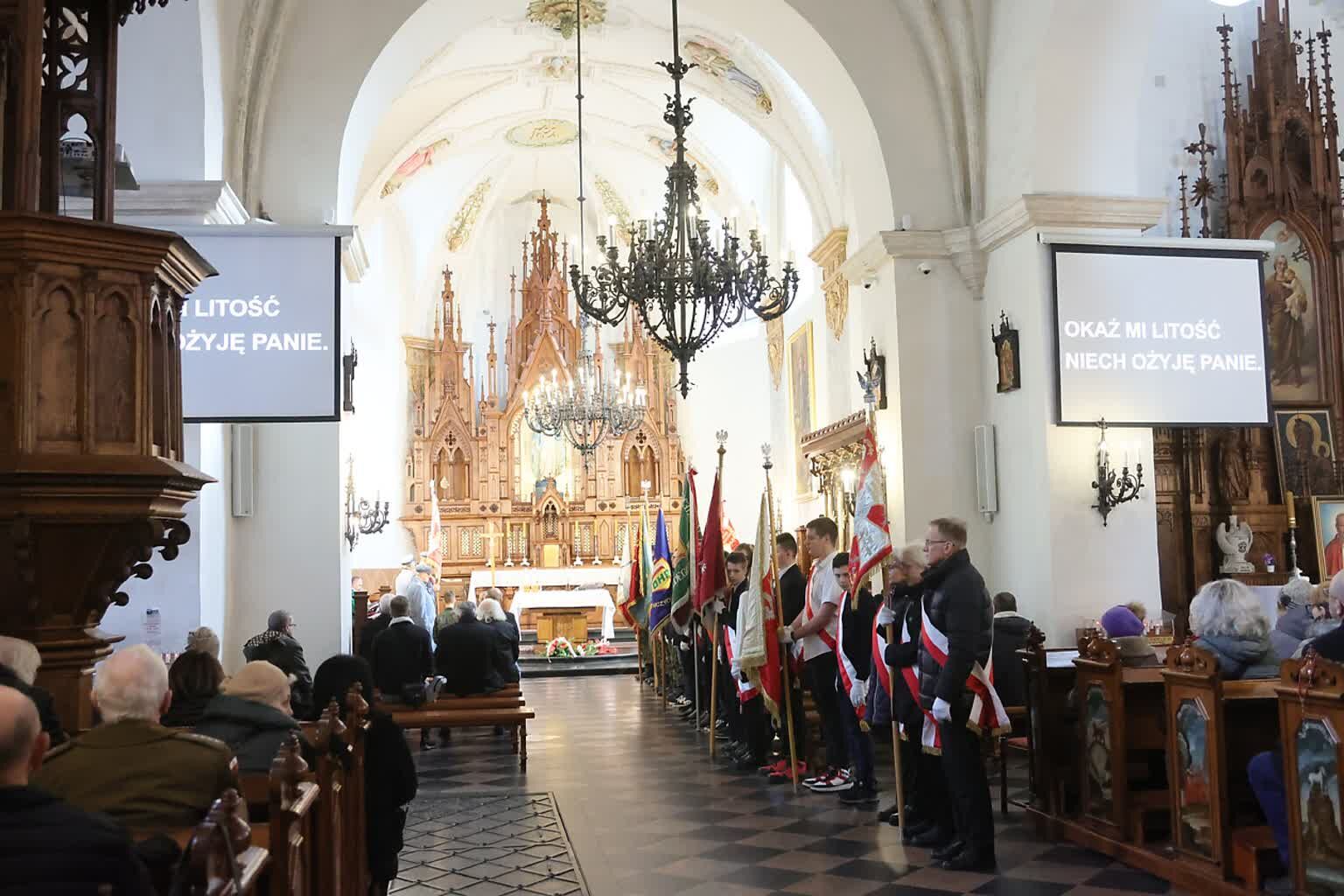 Wnętrze kościoła podczas uroczystości, z widocznymi chorągiewkami, zgromadzonymi ludźmi i ozdobnym ołtarzem w tle.