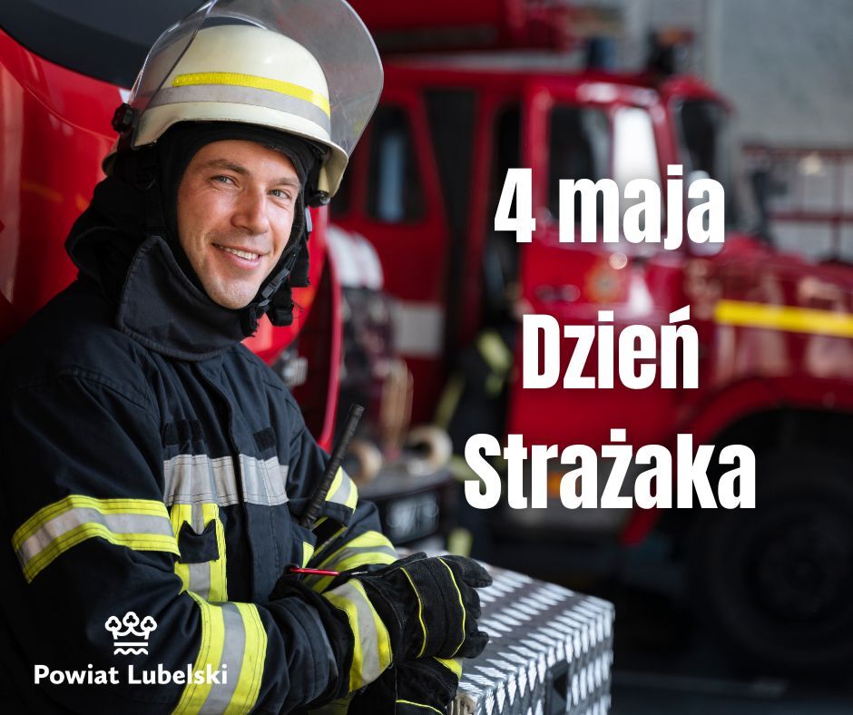 Strażak w hełmie i mundurze uśmiecha się, stojąc przed wozem strażackim. Obok niego napis: "4 maja Dzień Strażaka". Na dole logo Powiatu Lubelskiego.