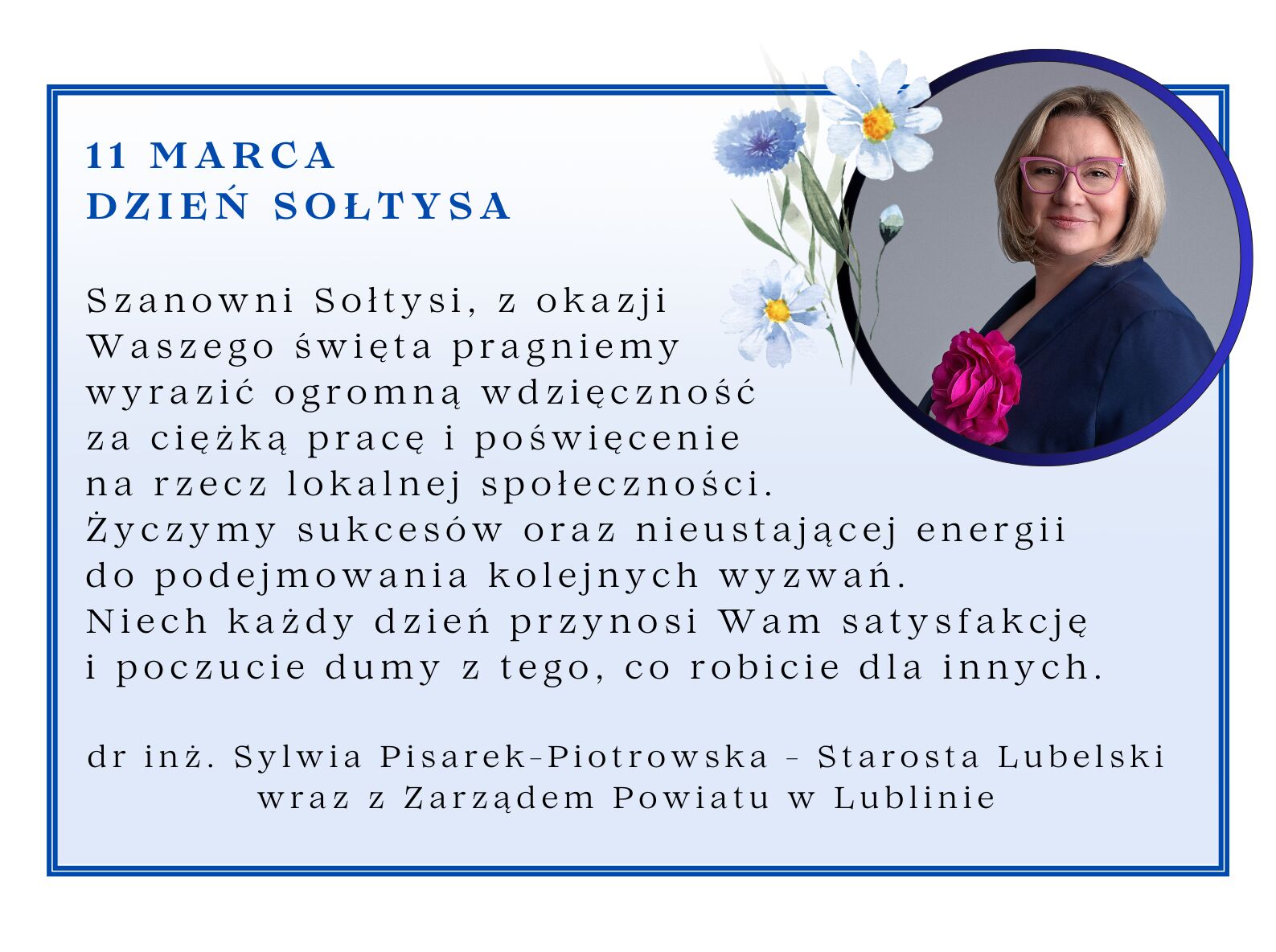 Z okazji Dnia Sołtysa kobieta w okularach i marynarce uśmiecha się na tle niebieskich kwiatów. Obok widoczny jest tekst z podziękowaniami i życzeniami od starosty lubelskiego.