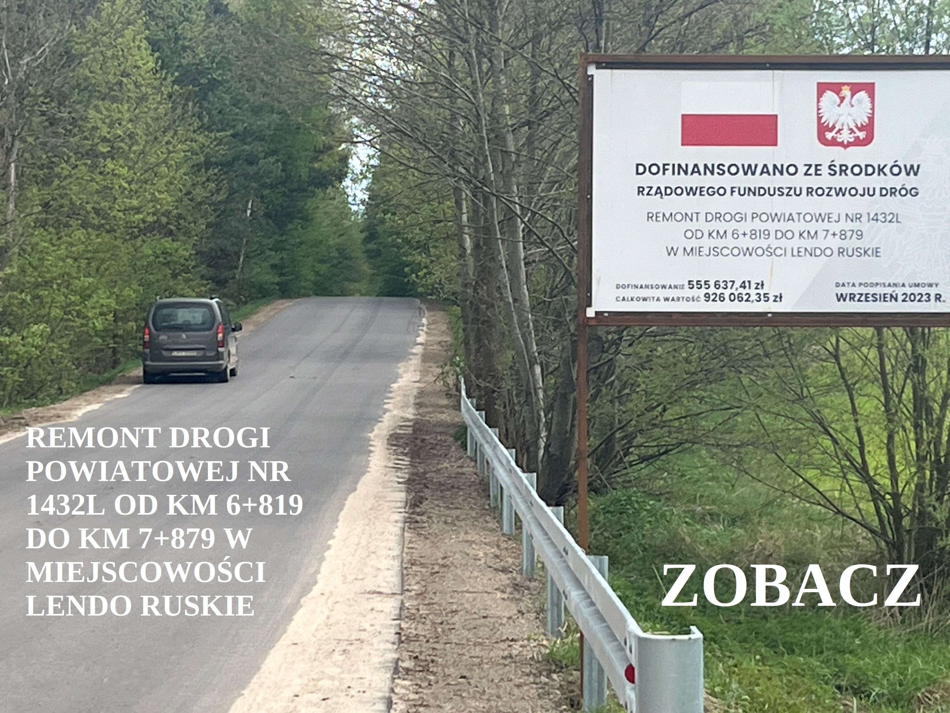 Ulica w otoczeniu zielonych drzew, po lewej stronie czerwono-białe ogrodzenie i znak informujący o remoncie drogi z herbem Polski.