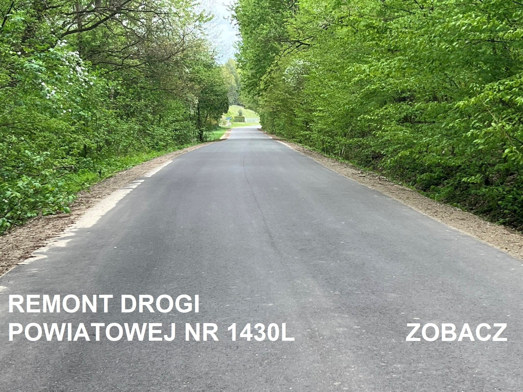 Nowo wyremontowany odcinek asfaltowej drogi powiatowej nr 1430L, otoczony zielenią drzew. Na asfalcie nadrukowany napis "REMONONT DROGI POWIATOWEJ NR 1430L ZOBACZ".