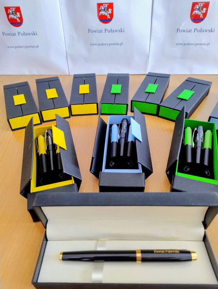 Zestaw długopis&oacute;w i pi&oacute;ro, tło herby Powiatu Puławskiego