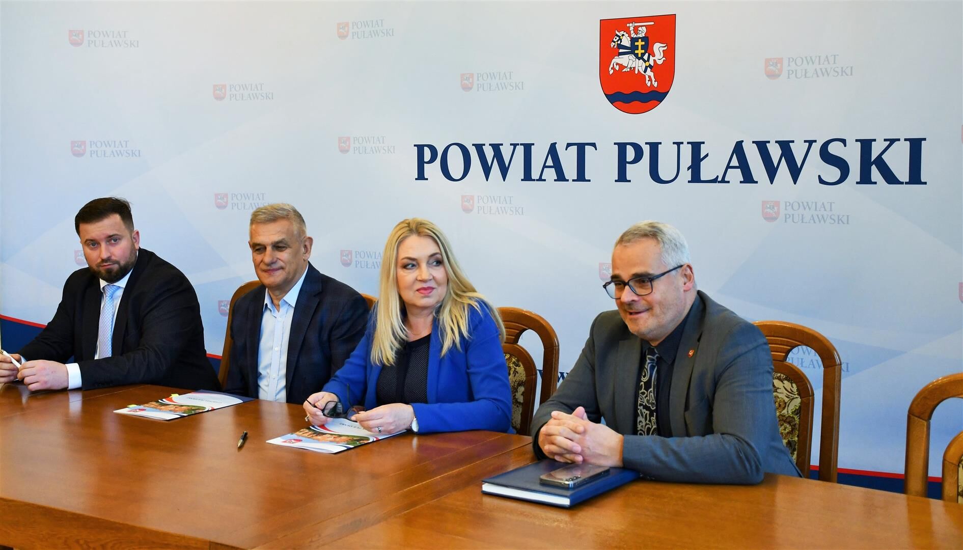 Podpisanie umowy dotacyjnej z Lokalną Organizacją Turystyczną Kraina Lessowych Wąwozów, za stołem przedstawicie powiatu i LOT. W tle ścianka z herbem powiatu.