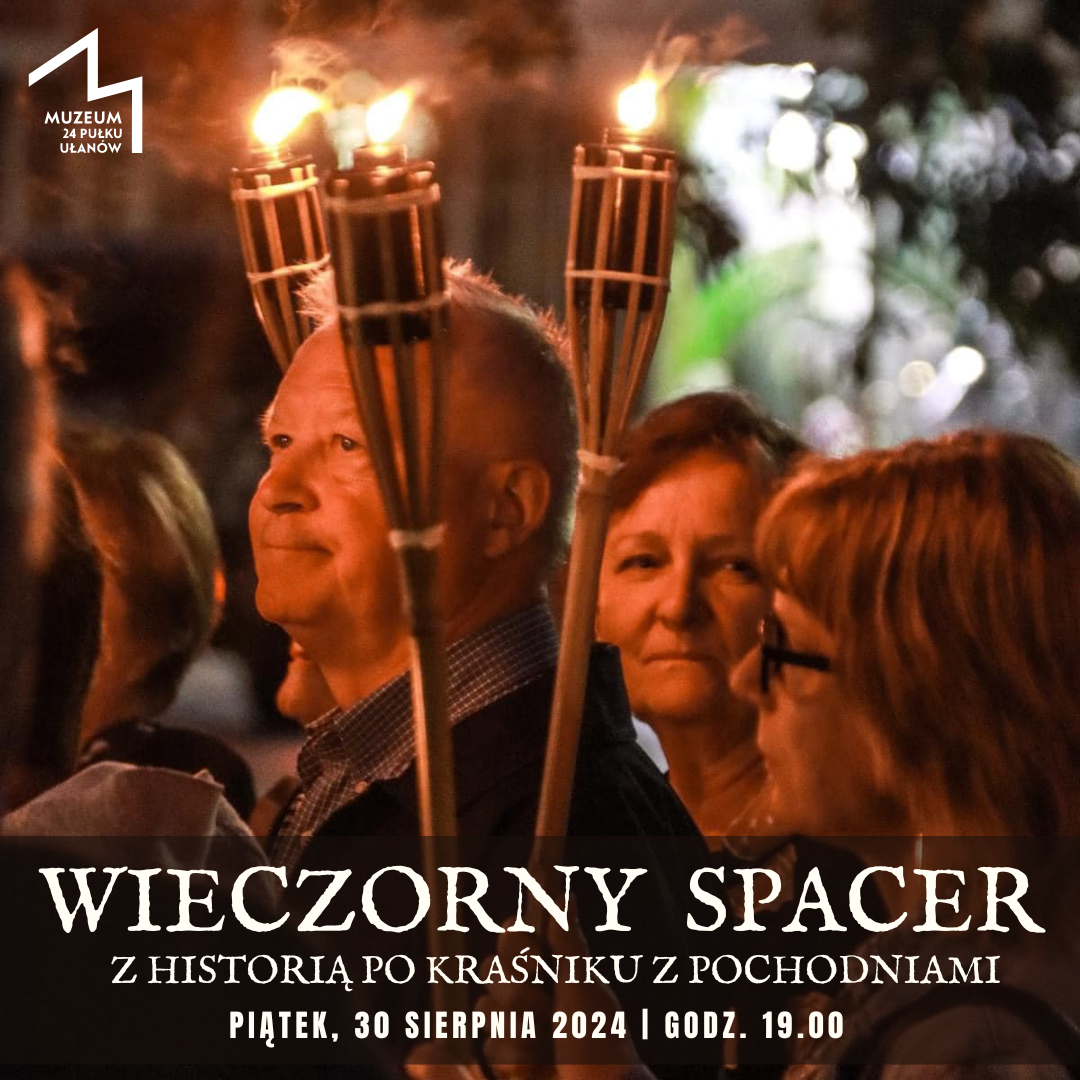 Zdjęcie przedstawia grupę osób uczestniczących w wieczornym spacerze z pochodniami. W tle widać ciemne niebo i roślinność. Na pierwszym planie wyróżnia się mężczyzna trzymający pochodnię.